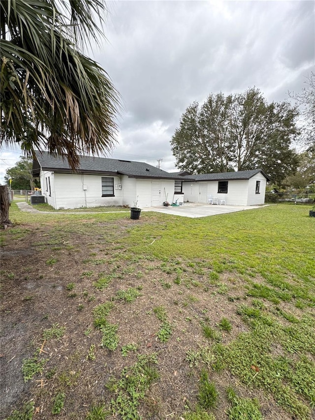 rear view of house featuring an attached garage, concrete driveway, a lawn, and a patio