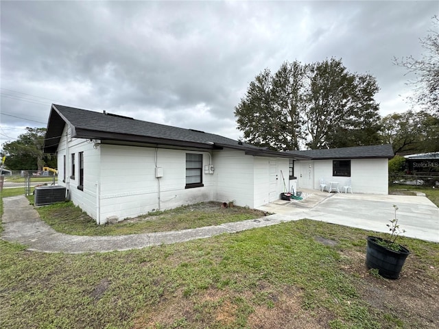 rear view of house featuring roof with shingles, a yard, central air condition unit, a patio area, and fence