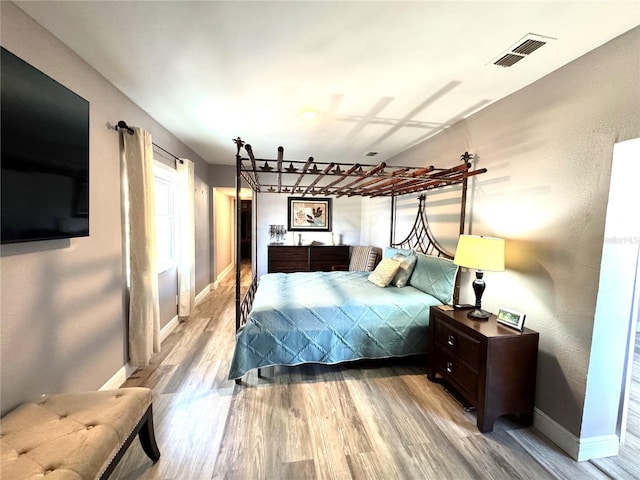 bedroom with baseboards, visible vents, and wood finished floors
