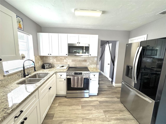 kitchen with light stone countertops, a sink, backsplash, white cabinets, and appliances with stainless steel finishes