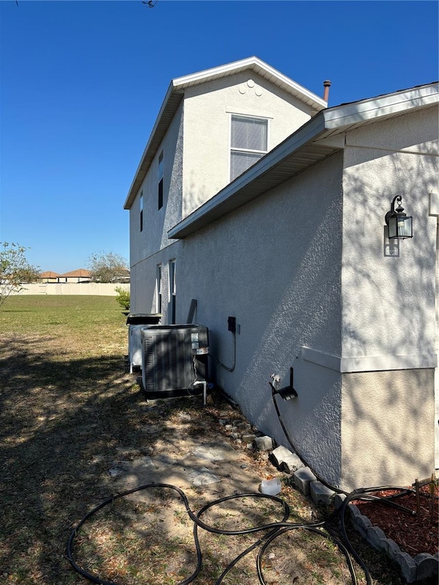 view of property exterior featuring stucco siding, a lawn, and central AC