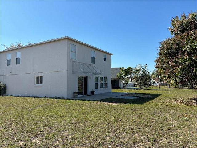 rear view of property with stucco siding, a lawn, and a patio area