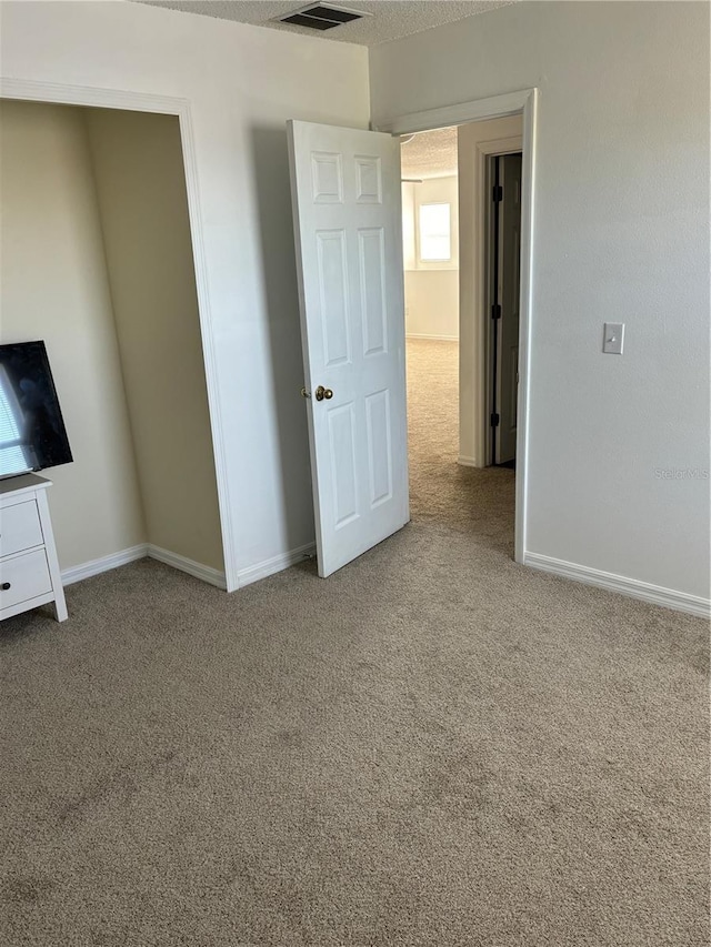 unfurnished bedroom featuring baseboards, carpet floors, a textured ceiling, and visible vents