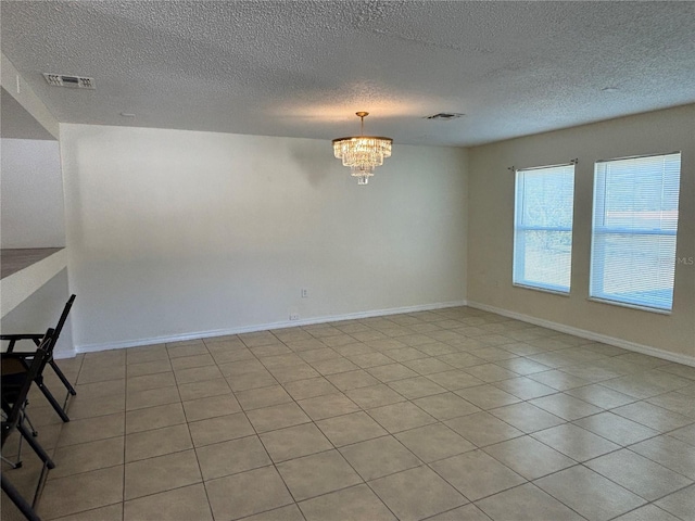 unfurnished room with visible vents, baseboards, a textured ceiling, and a chandelier