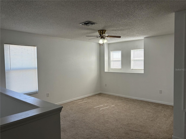 carpeted spare room featuring a ceiling fan, baseboards, visible vents, and a textured ceiling