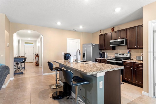 kitchen with arched walkways, dark brown cabinets, a breakfast bar area, and stainless steel appliances