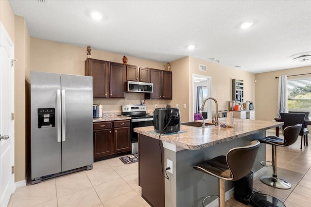 kitchen with visible vents, a sink, stainless steel appliances, dark brown cabinetry, and a kitchen breakfast bar