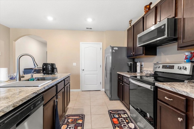 kitchen with visible vents, arched walkways, a sink, stainless steel appliances, and dark brown cabinetry