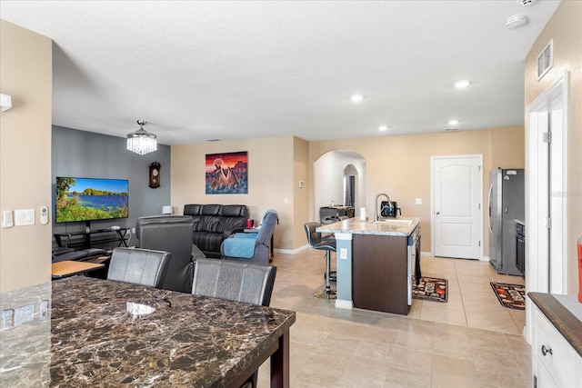 kitchen featuring a center island with sink, visible vents, arched walkways, freestanding refrigerator, and a sink