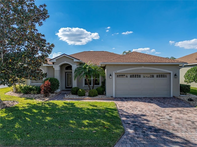 ranch-style home featuring a garage, a front lawn, decorative driveway, and stucco siding