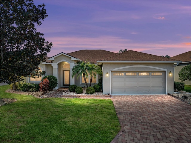 single story home featuring an attached garage, roof with shingles, decorative driveway, stucco siding, and a front lawn