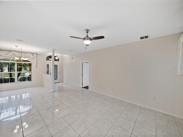 empty room with light tile patterned floors, ceiling fan with notable chandelier, visible vents, baseboards, and ornate columns