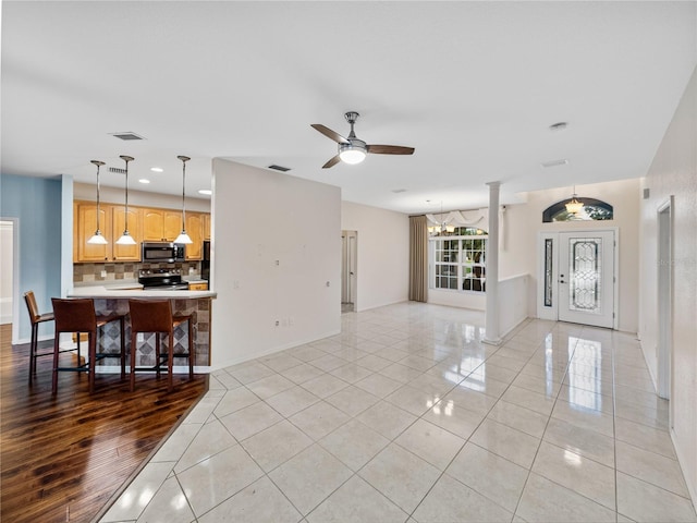 living room with ceiling fan with notable chandelier, light tile patterned floors, visible vents, and baseboards