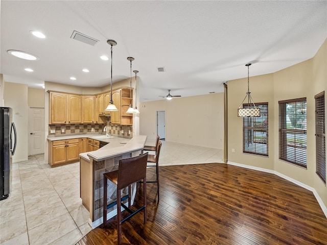 kitchen featuring tasteful backsplash, light brown cabinetry, open floor plan, a peninsula, and a kitchen bar