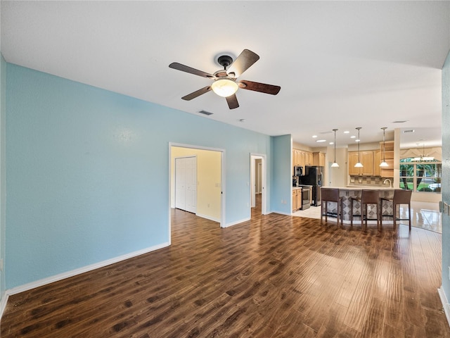 living room with ceiling fan with notable chandelier, dark wood-style flooring, visible vents, and baseboards