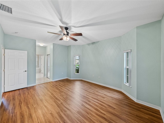 empty room featuring a ceiling fan, visible vents, baseboards, and wood finished floors