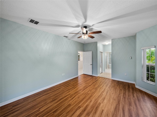 unfurnished bedroom with a textured ceiling, ensuite bath, wood finished floors, and baseboards