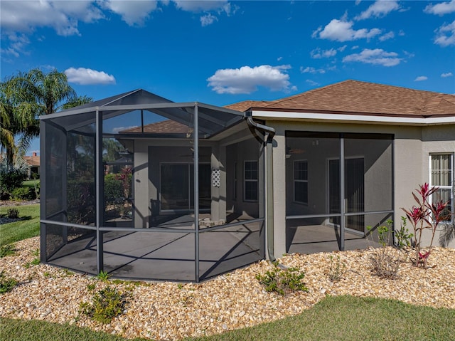 back of property with glass enclosure, a shingled roof, a patio, and stucco siding