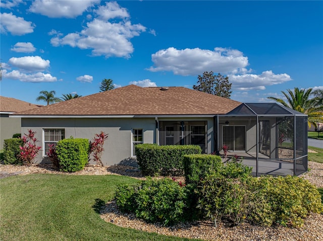 rear view of property featuring ceiling fan, glass enclosure, a shingled roof, a yard, and stucco siding