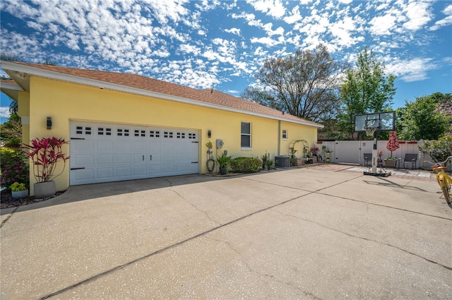 view of side of home with fence, driveway, central AC, stucco siding, and a garage