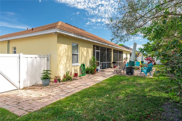 rear view of property with stucco siding, a patio, fence, a yard, and a sunroom