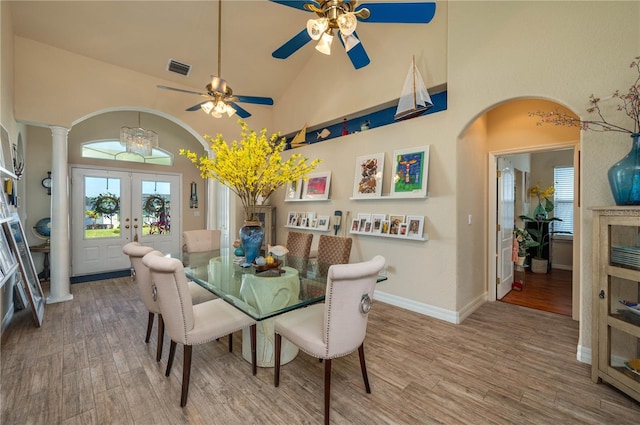 dining area featuring french doors, arched walkways, high vaulted ceiling, and wood finished floors