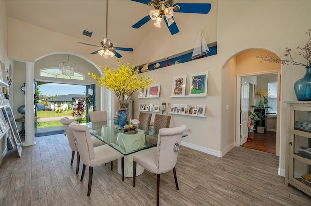 dining space featuring wood finished floors, visible vents, baseboards, high vaulted ceiling, and arched walkways