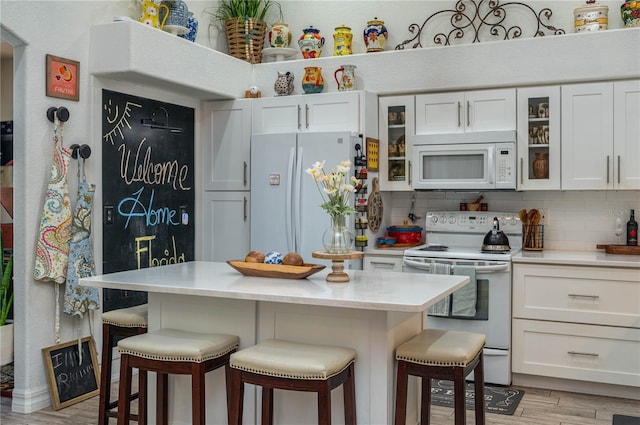 kitchen with a breakfast bar, white cabinetry, white appliances, light countertops, and decorative backsplash