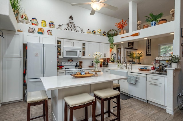 kitchen with glass insert cabinets, wood finish floors, a breakfast bar area, light countertops, and white appliances