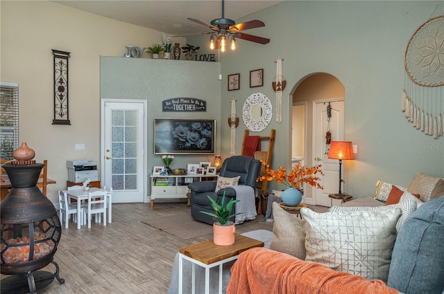 living room with arched walkways, a ceiling fan, light wood-style flooring, and a towering ceiling