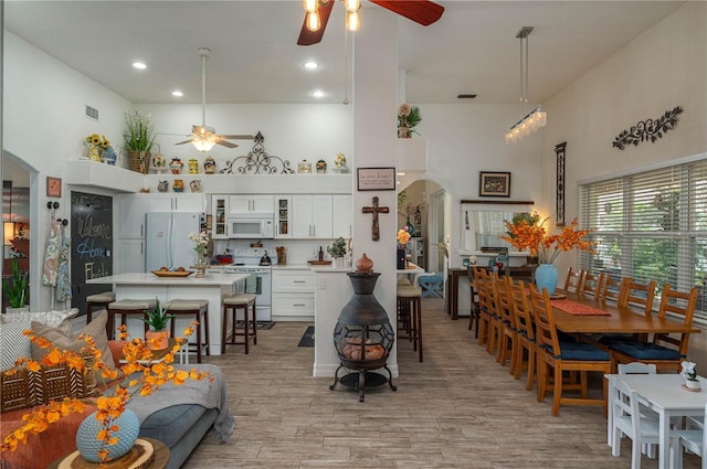 dining room with light wood finished floors, a ceiling fan, arched walkways, and a towering ceiling