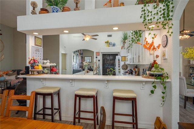 kitchen with wood finished floors, arched walkways, a breakfast bar, and ceiling fan