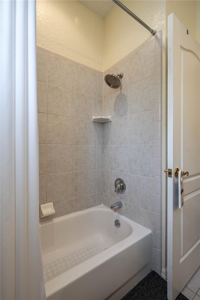 bathroom with washtub / shower combination and a textured wall