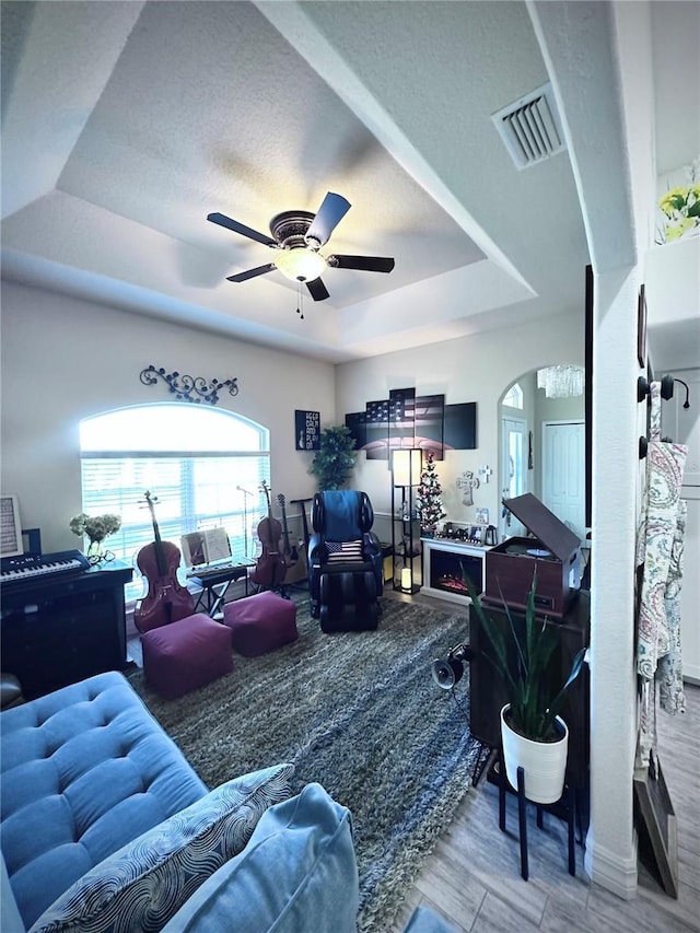 living room with visible vents, ceiling fan, wood finished floors, arched walkways, and a raised ceiling