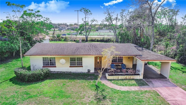 ranch-style home featuring roof with shingles, stucco siding, concrete driveway, a carport, and a front lawn