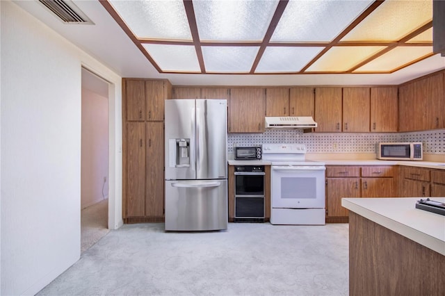 kitchen with white appliances, tasteful backsplash, brown cabinetry, light countertops, and under cabinet range hood