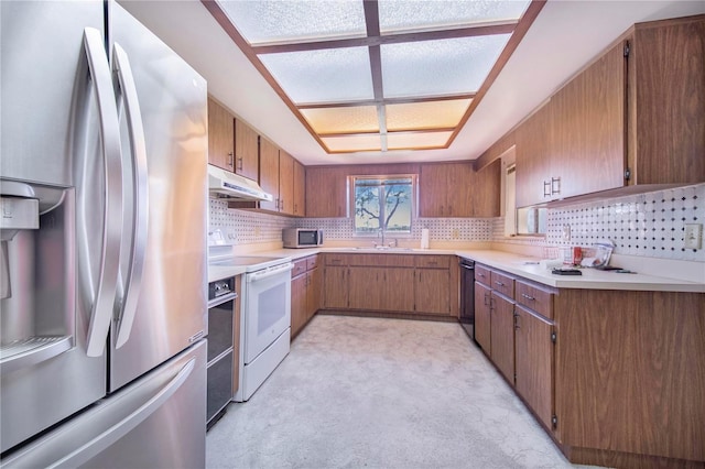 kitchen with decorative backsplash, brown cabinetry, appliances with stainless steel finishes, under cabinet range hood, and a sink