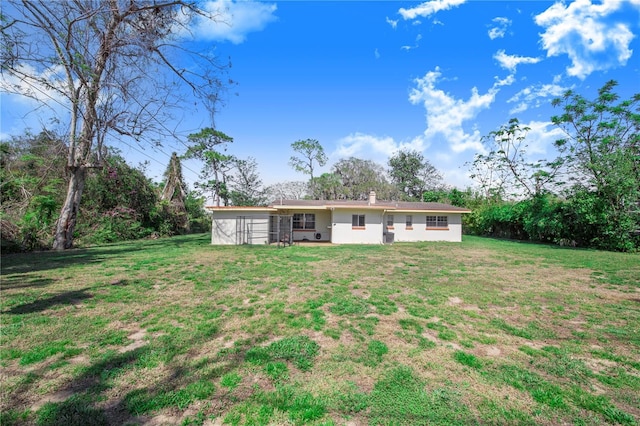 back of house featuring a lawn, a chimney, and stucco siding