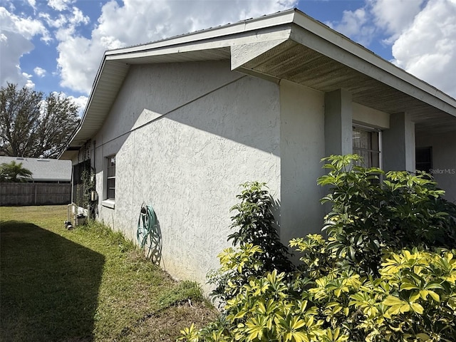 view of side of home with fence, a lawn, and stucco siding