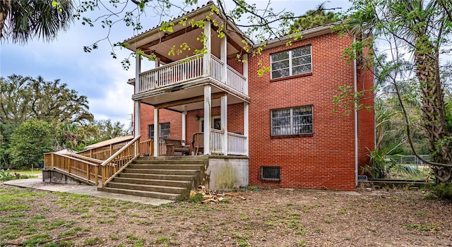 back of house with brick siding, a porch, and a balcony