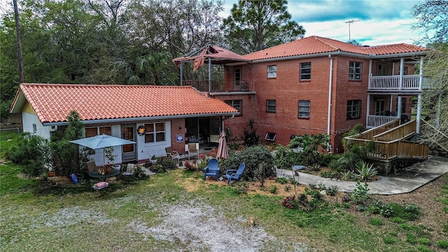 rear view of property featuring brick siding, a tiled roof, and a balcony