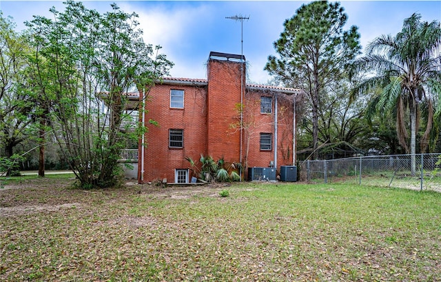 view of home's exterior with brick siding, a chimney, a lawn, central AC, and fence