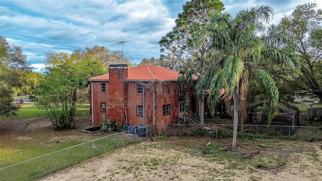 view of home's exterior featuring fence private yard, a chimney, brick siding, and a tiled roof