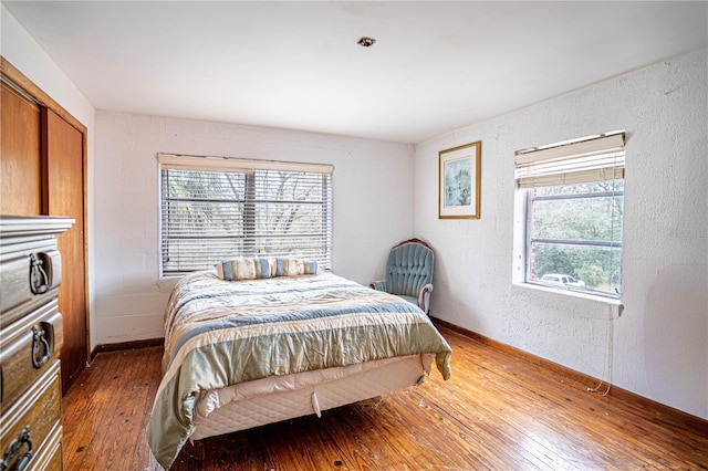 bedroom featuring wood-type flooring, baseboards, and a textured wall