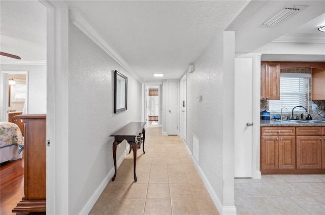 hall featuring baseboards, visible vents, a textured wall, crown molding, and a sink