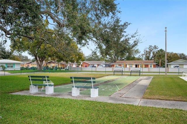 view of property's community with fence, shuffleboard, a lawn, and a residential view