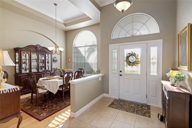 entrance foyer with a tray ceiling, a notable chandelier, light tile patterned floors, ornamental molding, and baseboards