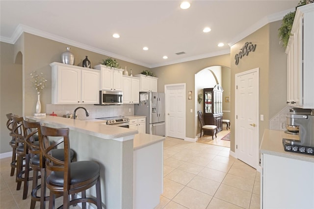 kitchen featuring arched walkways, a peninsula, appliances with stainless steel finishes, and a breakfast bar area