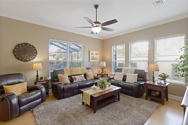 living room with light wood finished floors, ornamental molding, visible vents, and a ceiling fan