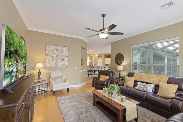 living area with light wood finished floors, visible vents, ornamental molding, ceiling fan, and baseboards